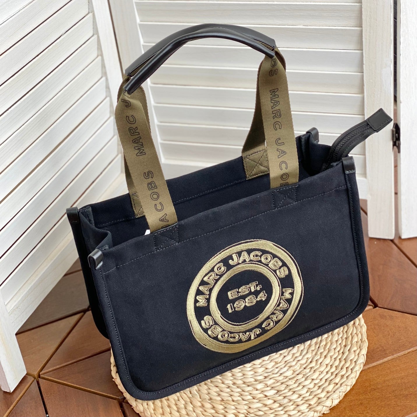 Black canvas tote bag with gold embroidered logo, khaki contrast handles, and zippered closure – a trendy yet functional everyday handbag
