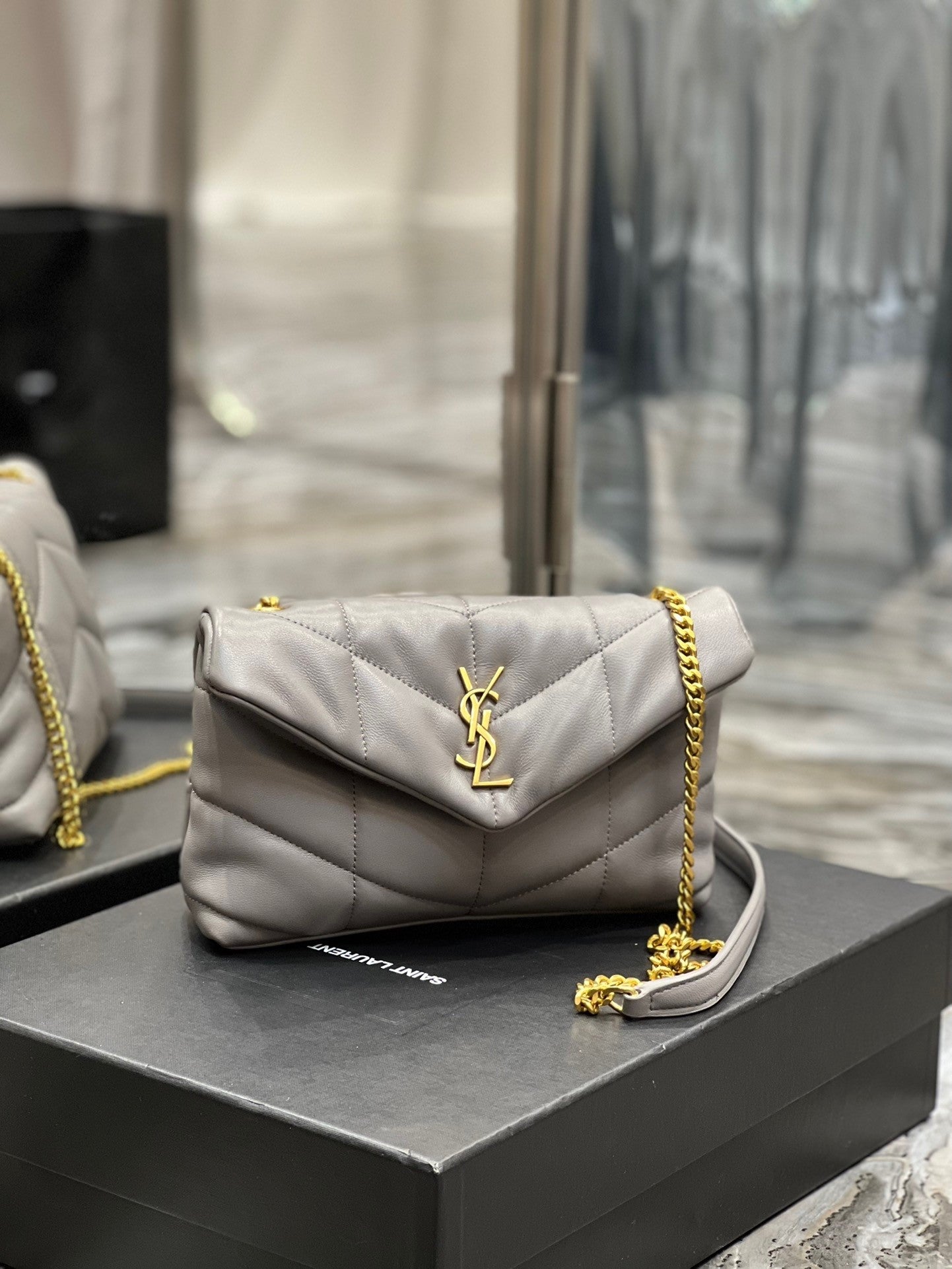  Gray quilted leather shoulder bag with gold-tone chain strap and soft, slouchy silhouette – a modern luxury accessory.