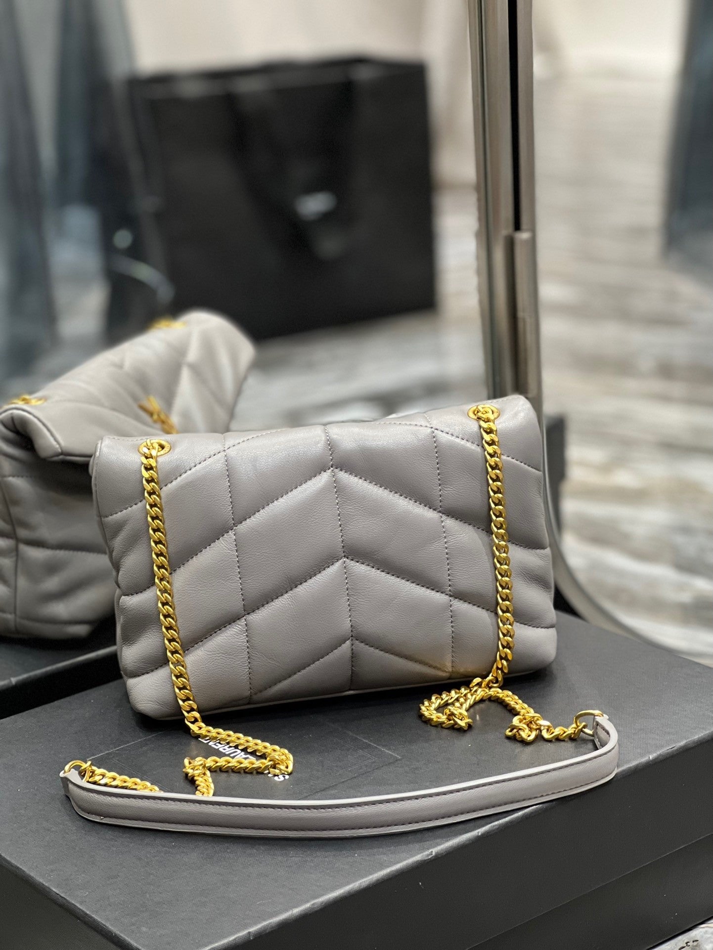  Gray quilted leather shoulder bag with gold-tone chain strap and soft, slouchy silhouette – a modern luxury accessory.
