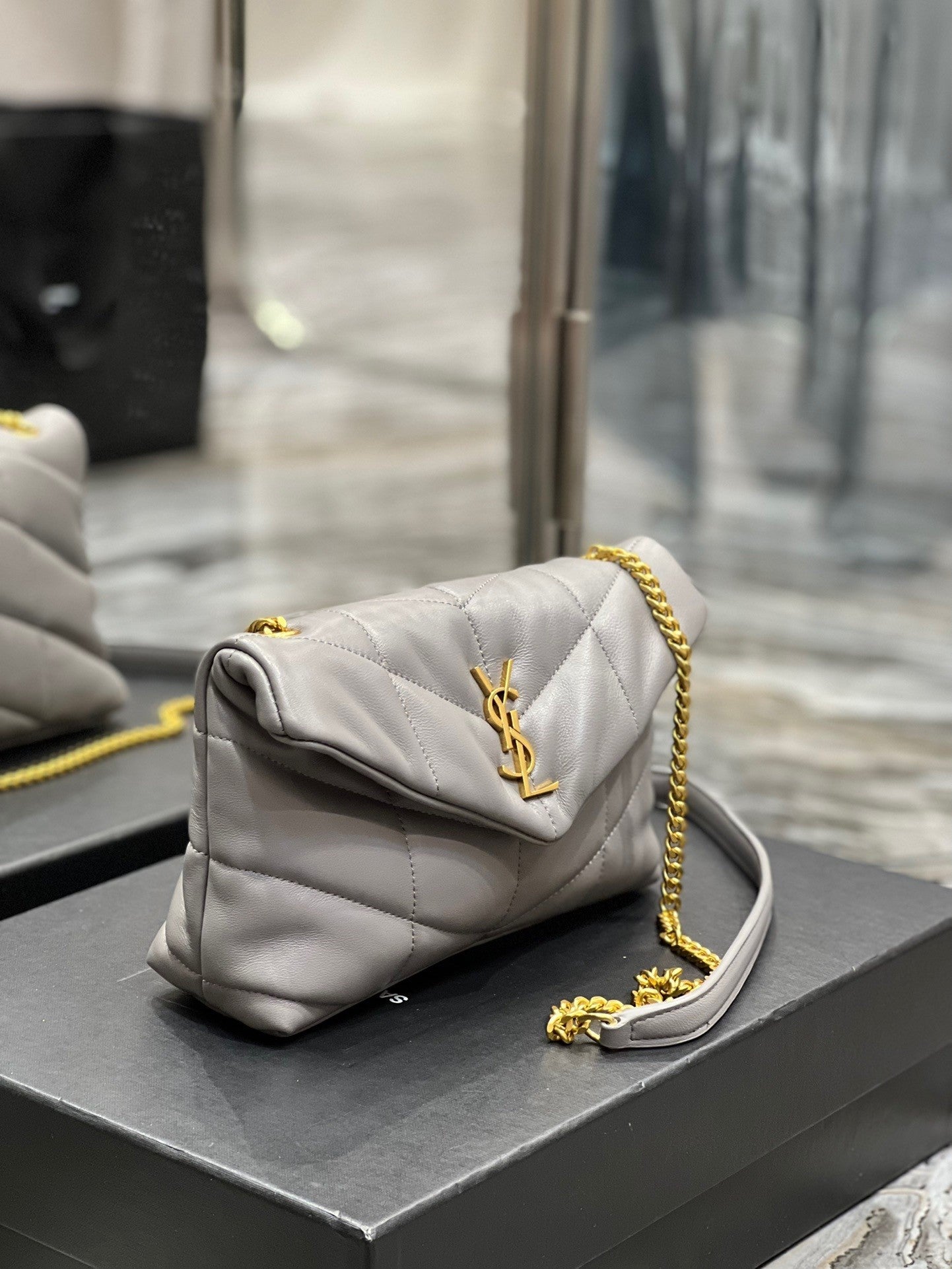  Gray quilted leather shoulder bag with gold-tone chain strap and soft, slouchy silhouette – a modern luxury accessory.