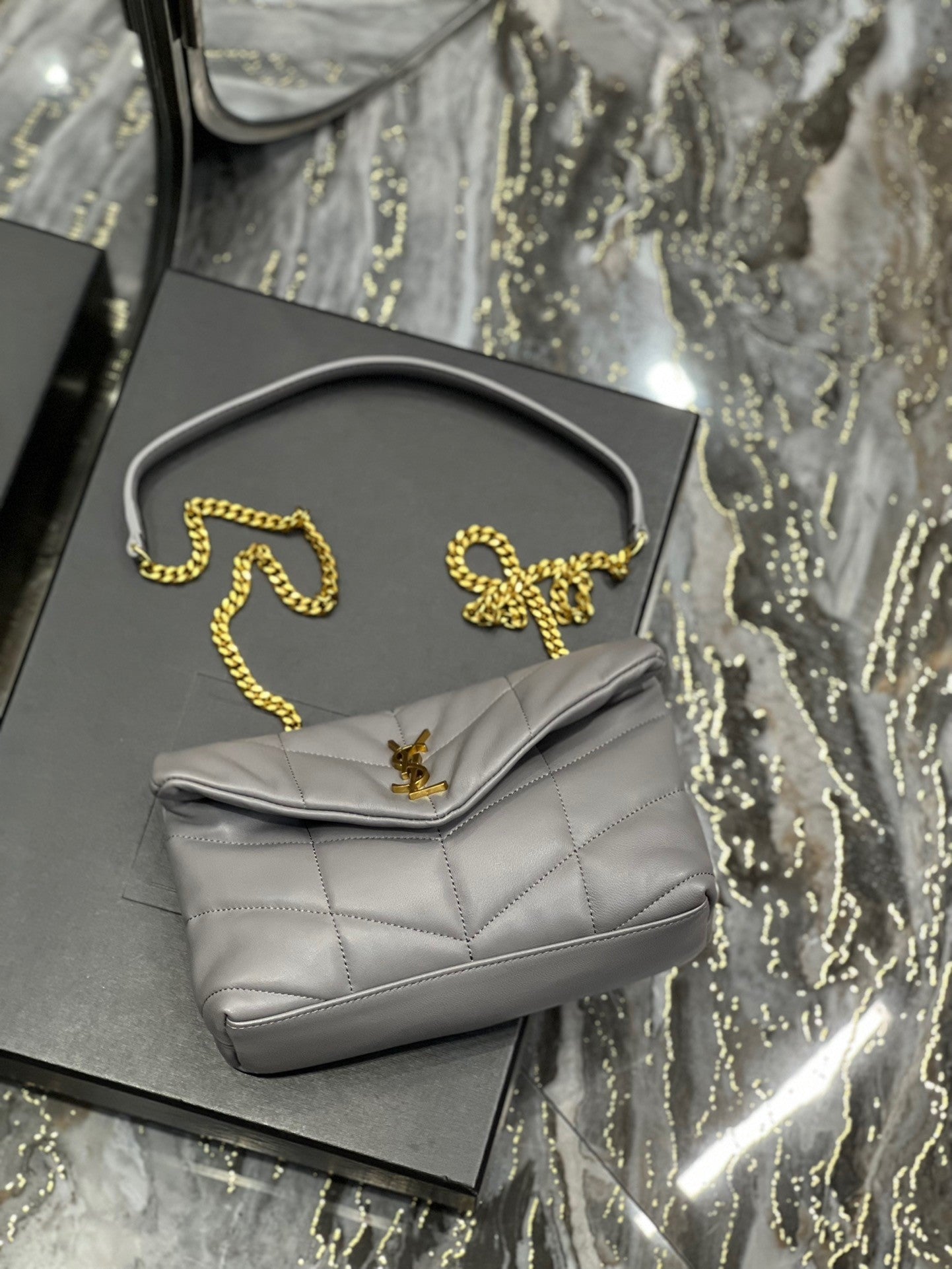  Gray quilted leather shoulder bag with gold-tone chain strap and soft, slouchy silhouette – a modern luxury accessory.