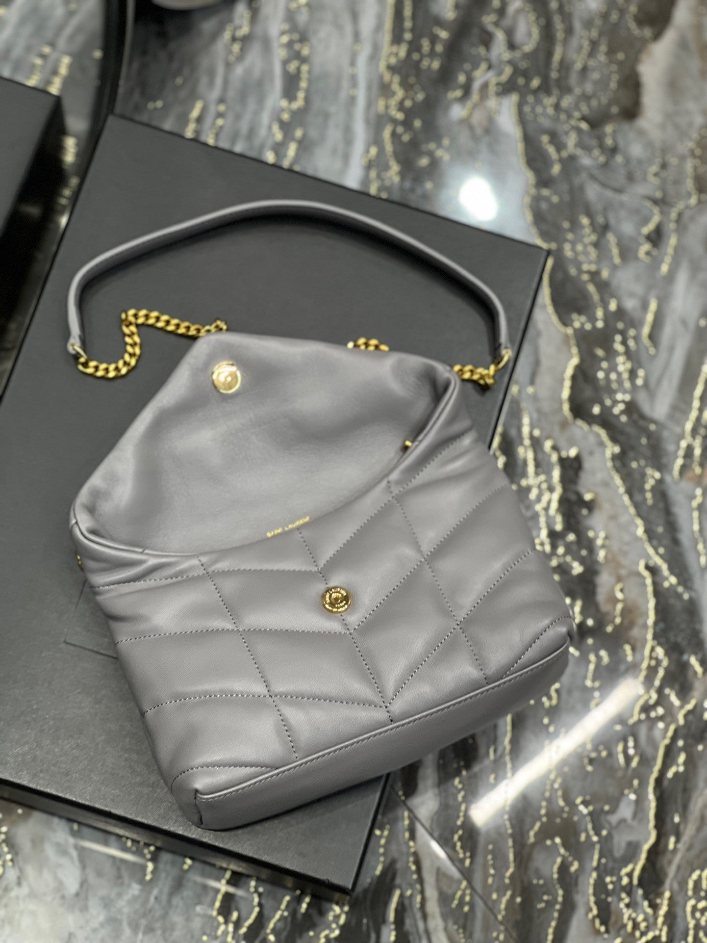  Gray quilted leather shoulder bag with gold-tone chain strap and soft, slouchy silhouette – a modern luxury accessory.